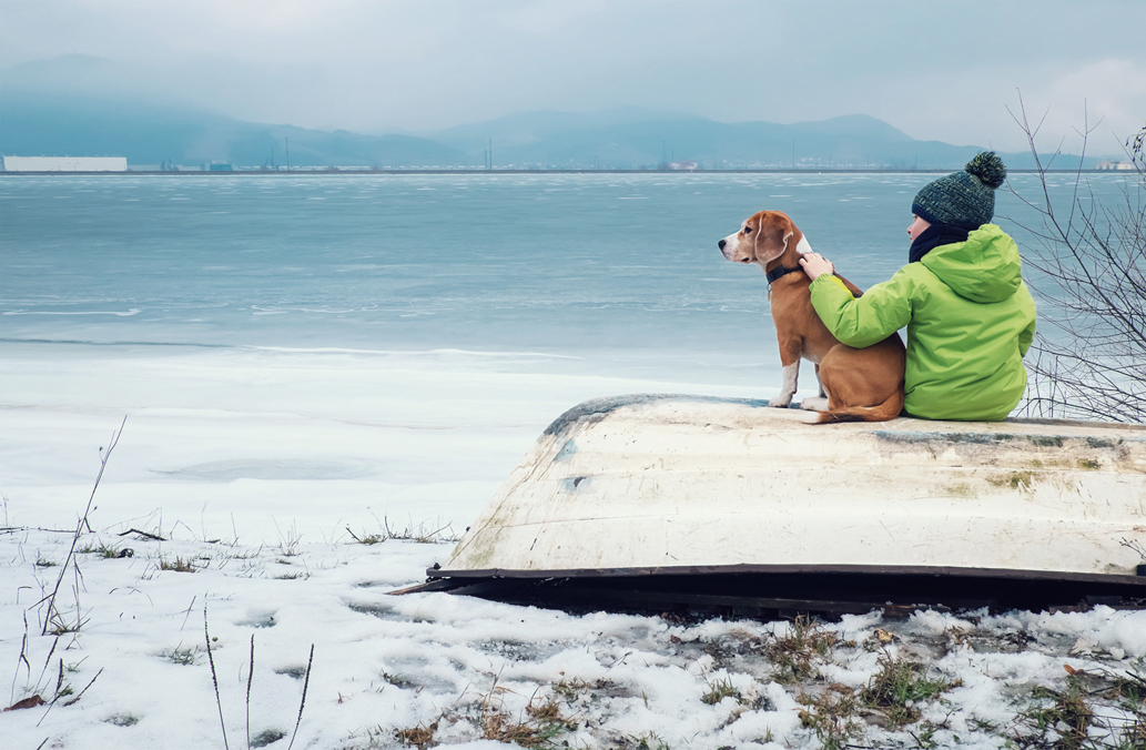 Boy with dog sitting together on the old boat near winter lake