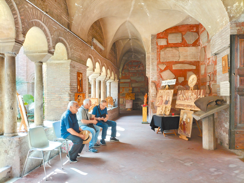 當地居民在教堂旁的修道院遺址舉辦美展，牆上鑲嵌著古建築遺跡。（作者攝影）